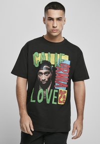 Camiseta de algodón negra con un gran gráfico de la cara de un hombre y texto en una fuente negrita y multicolor. Manga corta, corte casual.
