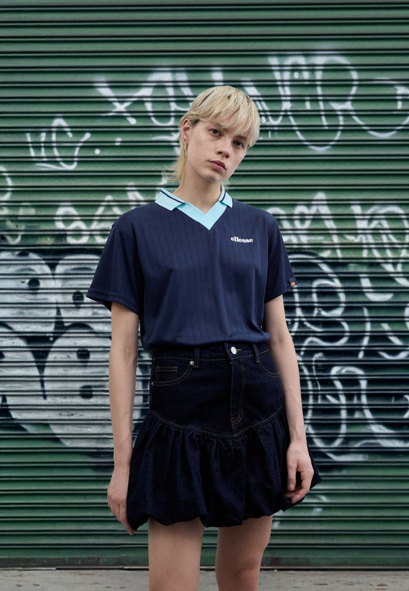 Nāvzils sportiska stila krekls ar gaiši zilu apkakli, kombinēts ar tumšu džinsa svārku ar volānveida apmali un kabatu detaļām.