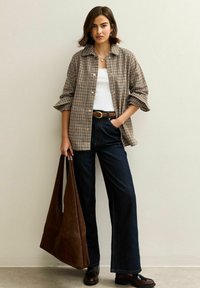 Brun rutig oversized skjorta, vit linne, högmidjade mörka jeans, brun läderbälte och en stor brun mocka tote-väska.
