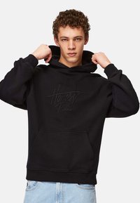 Svart huvtröja i mjukt tyg med en framficka och präglad text "Ärlighet Råder". Avslappnad passform med ribbade mudd och nederkant.