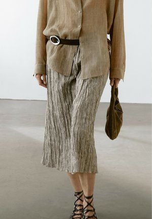 Chemise en lin beige à fermeture par boutons et manches longues, associée à un pantalon plissé texturé gris clair et une pochette en tissu marron.