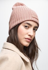 Beanie rosa a maglia con texture a coste e risvolto, caratterizzato da un piccolo patch in pelle rettangolare sul fronte.