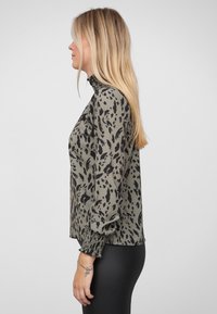 Olivengrøn bluse med sort abstrakt print, høj rynket krave og pufærmer. Glat, let stof med rynkede manchetter.