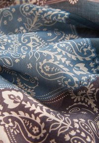 Tissu bleu et marron avec des motifs floraux et cachemire blancs détaillés, doucement plié montrant la texture et les détails du design.