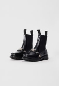 Bottines en cuir noir avec des semelles épaisses, des panneaux latéraux élastiques, des languettes de tirage et des chaînes décoratives en métal argenté à l'avant.