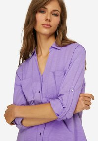 Camicia a maniche lunghe color lavanda con colletto a bottoni, due tasche frontali, maniche arrotolate e una finitura in tessuto texturizzato.