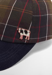 Καπέλο μπέιζμπολ με πλάγιες ρίγες σε σκούρες αποχρώσεις και δομημένο ναυτικό γείσο. Διαθέτει ένα μεταλλικό γαλάζιο πίν σε πλευρά, προσθέτοντας μια μοναδική λεπτομέρεια.