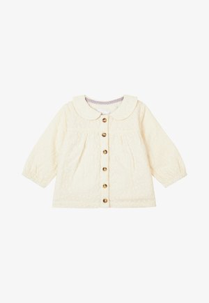 Cremefarvet quiltet jakke med Peter Pan-krave, knaplukning foran og lange ærmer. Har en diskret blomstret tekstur og gyldne knapper.