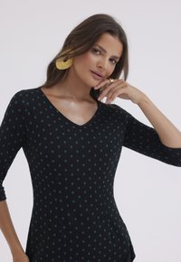Czarny top z rękawami o długości trzech czwartych, z dekoltem w kształcie V i turkusowymi kropkami. Gładka tekstura, dopasowany krój i detale w postaci bocznych kieszeni.