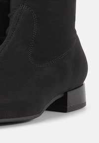 Μαύρο μποτάκι αστραγάλου με λεία, ματ επιφάνεια, που διαθέτει τετράγωνο τακούνι και διακριτικές ραφές. Το υλικό φαίνεται ανθεκτικό και στιβαρό.