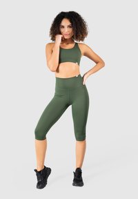Reggiseno sportivo verde oliva e leggings capri a vita alta realizzati in materiale elasticizzato. Abbinati a scarpe sportive nere.
