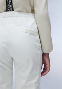 White waterproof pants with a textured surface, elastic waistband, and logo patch on the back pocket. Fleece top with gathered sleeves.