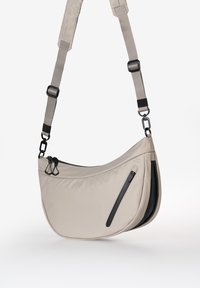 Borsetta a tracolla in nylon beige chiaro con design curvo. Presenta una tasca con zip nera e una tracolla regolabile con dettagli in metallo neri.