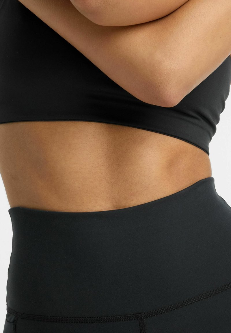 Haut de sport noir à texture lisse, présentant un design court et une taille haute, souligné par des détails de couture subtils.