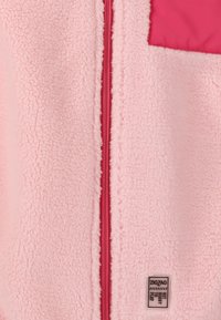 Fleece takki pehmeässä vaaleanpunaisessa, jossa on keskusvetoketju vaaleanpunaisilla yksityiskohdilla ja neliömäinen rintatasku. Sisältää brändilapun alareunassa.