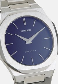 Montre en acier inoxydable argenté avec un boîtier octogonal, un cadran bleu, de fines aiguilles des heures et des minutes argentées, et des index des heures minimalistes.