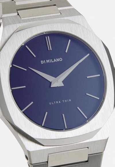 Strieborné nerezové hodinky s oktagónovým puzdrom, modrým ciferníkom, tenkými striebornými hodinovými a minútovými ručičkami a minimalistickými hodinovými značkami.