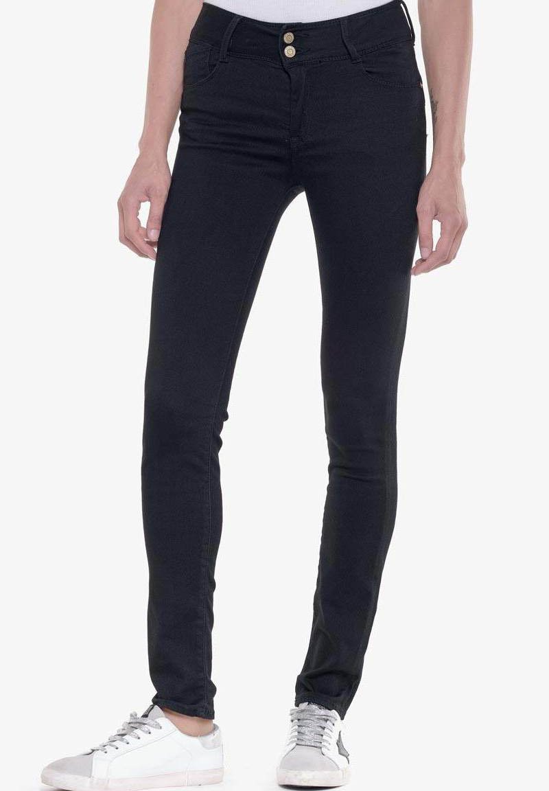Jeans ajustados negros de mezclilla, con una cintura de altura media, dos bolsillos frontales, dos bolsillos traseros y dos botones frontales. Combinados con zapatillas blancas.