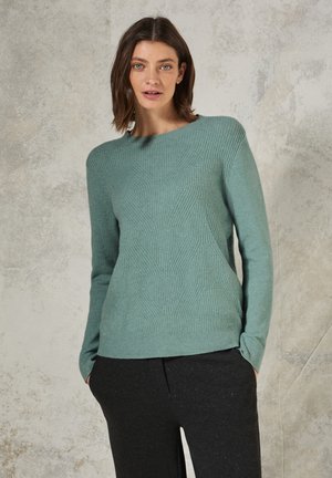 Turquoise knitted sweater with a textured diamond pattern, crew neckline, and long sleeves, paired with dark, tapered pants.