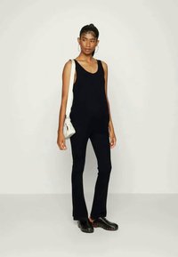 Top preto sem mangas combinado com calças pretas justas. O conjunto é complementado por tamancos pretos com acabamentos metálicos e uma bolsa de ombro branca.