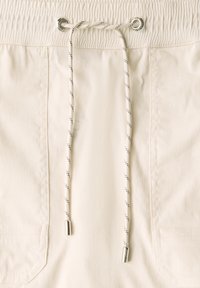 Shorts couleur crème avec une taille élastique, dotés d'un cordon de serrage avec des motifs noir et blanc et des œillets en métal argenté pour l'ajustement.