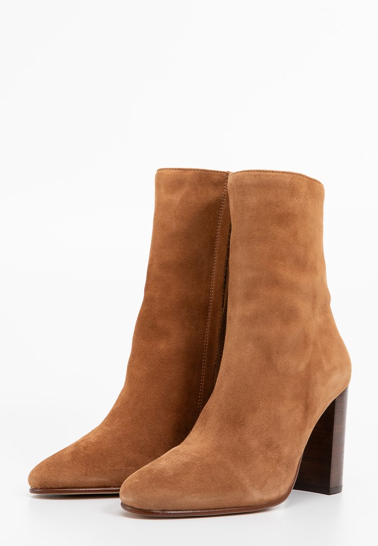 Bottines en suède brun avec un bout pointu, une couture verticale et un talon en bois large. La tige a une texture lisse et douce.