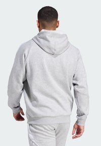 Grå hettegenser med en myk tekstur, med hette, ribbestrikkede mansjetter og linning; kombinert med matchende grå joggebukser og hvite sidestrimler.