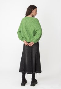 Žalias megztinis su tekstūruotais deimanto raštais, derinamas su juodu džinsiniu midi sijonu. Modelis vilki juodas raukšlėtas kojines ir masyvius batus.