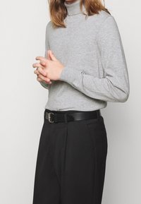 Maglione grigio a collo alto, texture in maglia morbida, maniche lunghe, abbinato a pantaloni neri e una cintura di pelle con una fibbia argentata.