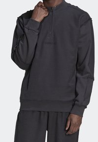 Svart pulloversweatshirt med halvdragkedja, ribbade muddar och en texturerad yta. Funktioner "adidas"-logotyp i matchande färg.