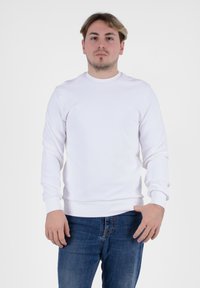 Felpa bianca a maniche lunghe con collo a giro. Tessuto morbido, abbinata a jeans blu scuro. Design semplice senza fantasie.