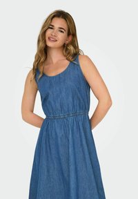 Denim bešvarkis su apvaliu iškirpimu, elastinga juosta ir plačiu sijonu, vidutinio mėlynumo spalvos su minkšta tekstūra.