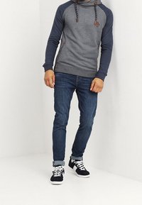 Szary i granatowy hoodie ze sznurkiem, skórzanymi akcentami i kieszenią kangurką, w połączeniu z ciemnymi dżinsami i czarnymi sneakerami.