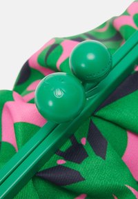 Fermoir vert avec une abeille embossée et le texte "Weekend" sur un fond de tissu coloré aux motifs verts, roses et noirs.