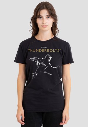 Young woman wearing black Marvel Thunderbolts t-shirt featuring a hooded character in action with a shield on gray background.