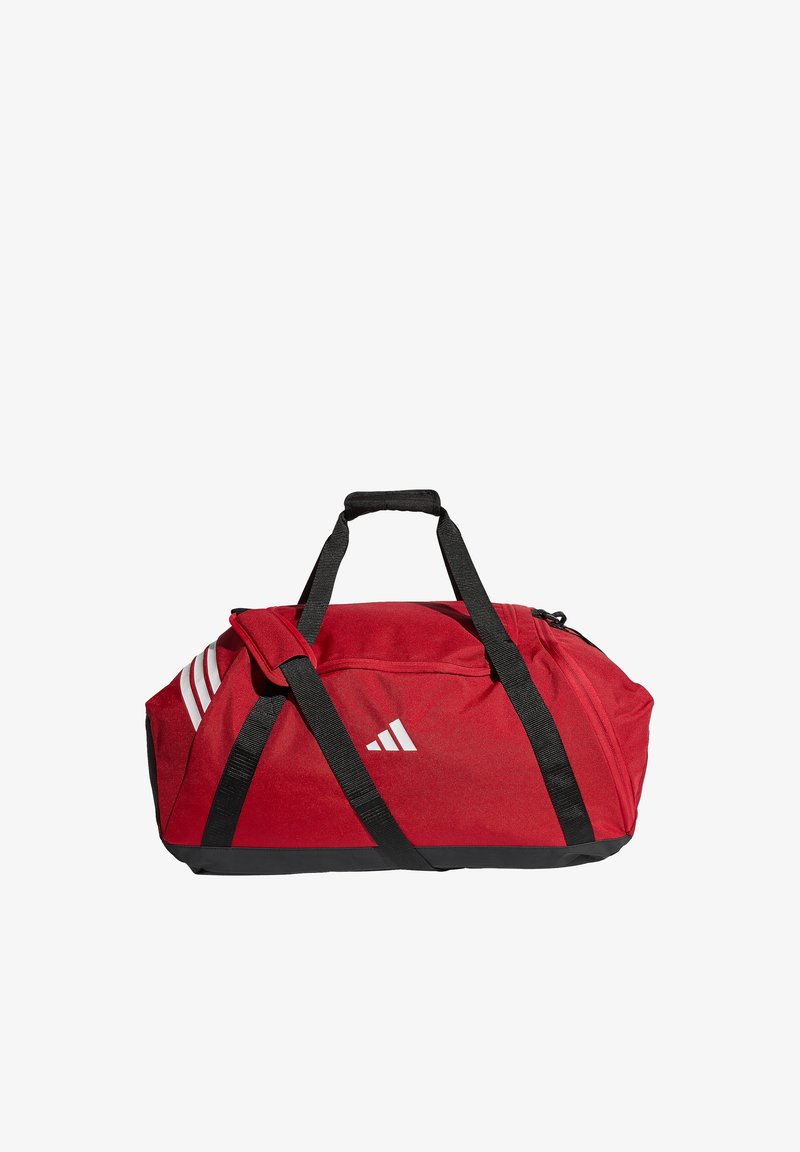Κόκκινη αθλητική τσάντα τύπου duffel με μαύρες λαβές και ιμάντα ώμου, λευκό λογότυπο Adidas στη πλευρά και λευκές τρεις ρίγες στην τσέπη στο τέλος.