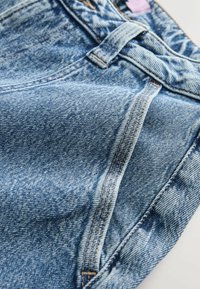 Heledad pesue denim teksad sirge lõikega, nähtava esikoti, kontrastse heledat pruunist õmblusega ja kergete tekstuurikõikudega.