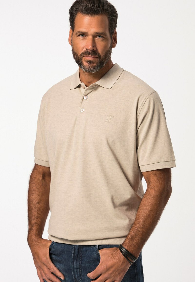 Béžové polo tričko s krátkým rukávem, límečkem, třemi knoflíky a jemným logem. Nosené s tmavě modrými džíny.