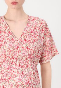 Rochie florală cu decolteu în V, mâneci scurte cu volane, talie elastică și un model de flori roz și roșii pe un fundal deschis.