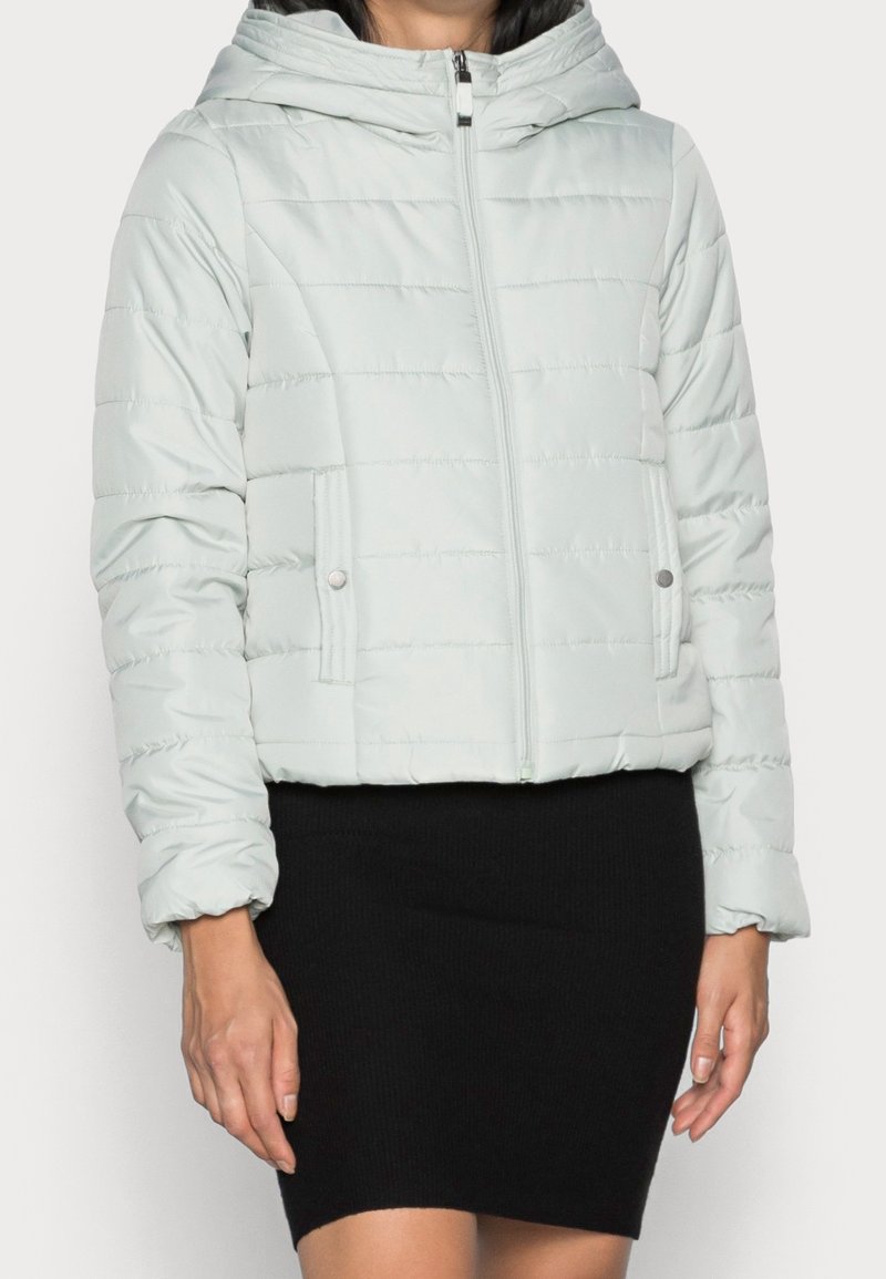 Jasnoszara kurtka puchowa z kapturem, zapinana na zamek błyskawiczny, z ściągaczami na rękawach. Posiada poziome przeszycia oraz dwie boczne kieszenie.