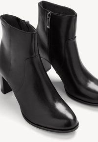 Bottines en cuir noir avec une finition lisse, des talons carrés et des fermetures éclair sur le côté. Elles présentent un bout pointu et un design minimaliste.