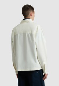 Lichtgekleurde shirt met een gestructureerde kraag, lange mouwen en een rugpasse. Gladde stof met een relaxte pasvorm en knoopmanchetten.