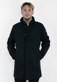 Abrigo negro impermeable con un alto cuello, botones en el frente, bolsillos laterales y un parche con el logo en la manga izquierda. Textura suave, hasta la rodilla.