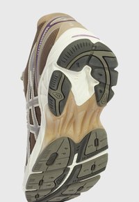 Semelle d'une chaussure de sport marron et beige avec une bande de roulement en caoutchouc texturé, une semelle intermédiaire blanche et des accents violets visibles sur la partie supérieure.
