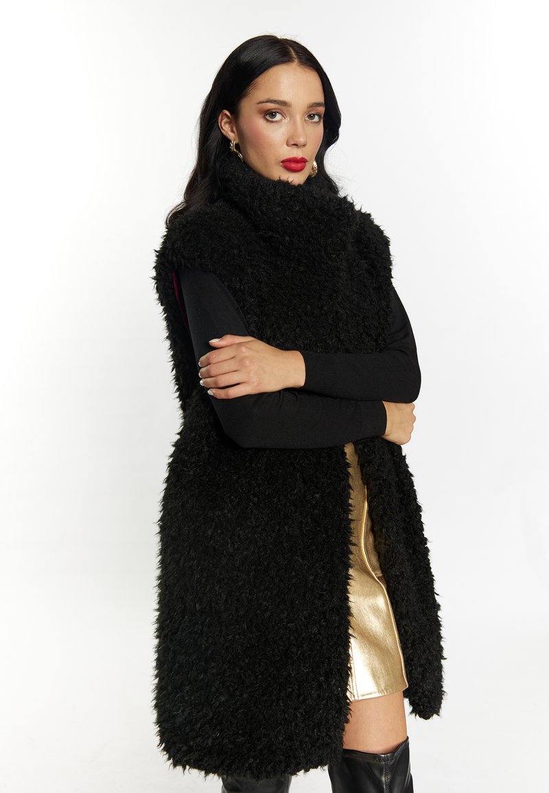Zwart harig faux fur zonder mouwen vest, hoge kraag, gecombineerd met een strak zwart langslijvig top en een gouden metallic minirok. Zwart knielaarzen.