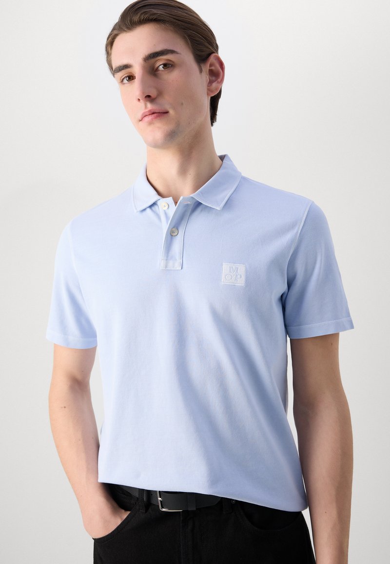 Hellblaues Poloshirt aus Baumwolle mit einem kleinen gestickten Logo auf der Brust, einem Zwei-Knopf-Halsbündchen und kurzen Ärmeln.