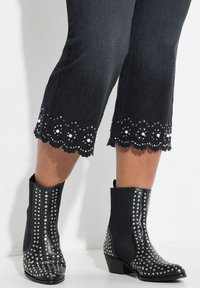 Bottines noires avec un design clouté, présentant des clous en métal le long de la tige et des orteils. Le dessous a un petit talon empilé.