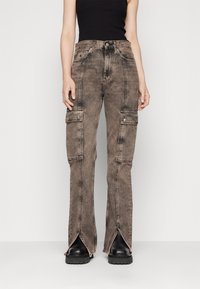 Pantalones cargo de denim marrón desgastado, con dos bolsillos laterales, piernas acampanadas y dobladillos abiertos, combinados con botas de plataforma negras.