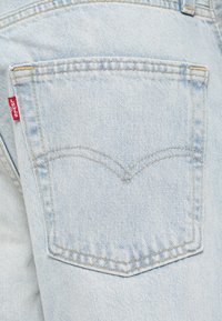 Jeans de mezclilla azul claro que presentan un bolsillo trasero visible con una etiqueta roja de Levi's y un patrón de costura curvada característico sobre el bolsillo.