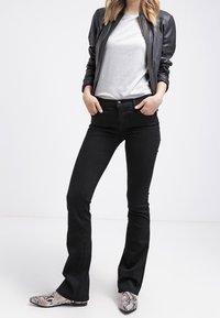 Black flared jeans with a smooth texture, worn with a grey t-shirt and a black leather jacket; paired with grey snakeskin-patterned shoes.